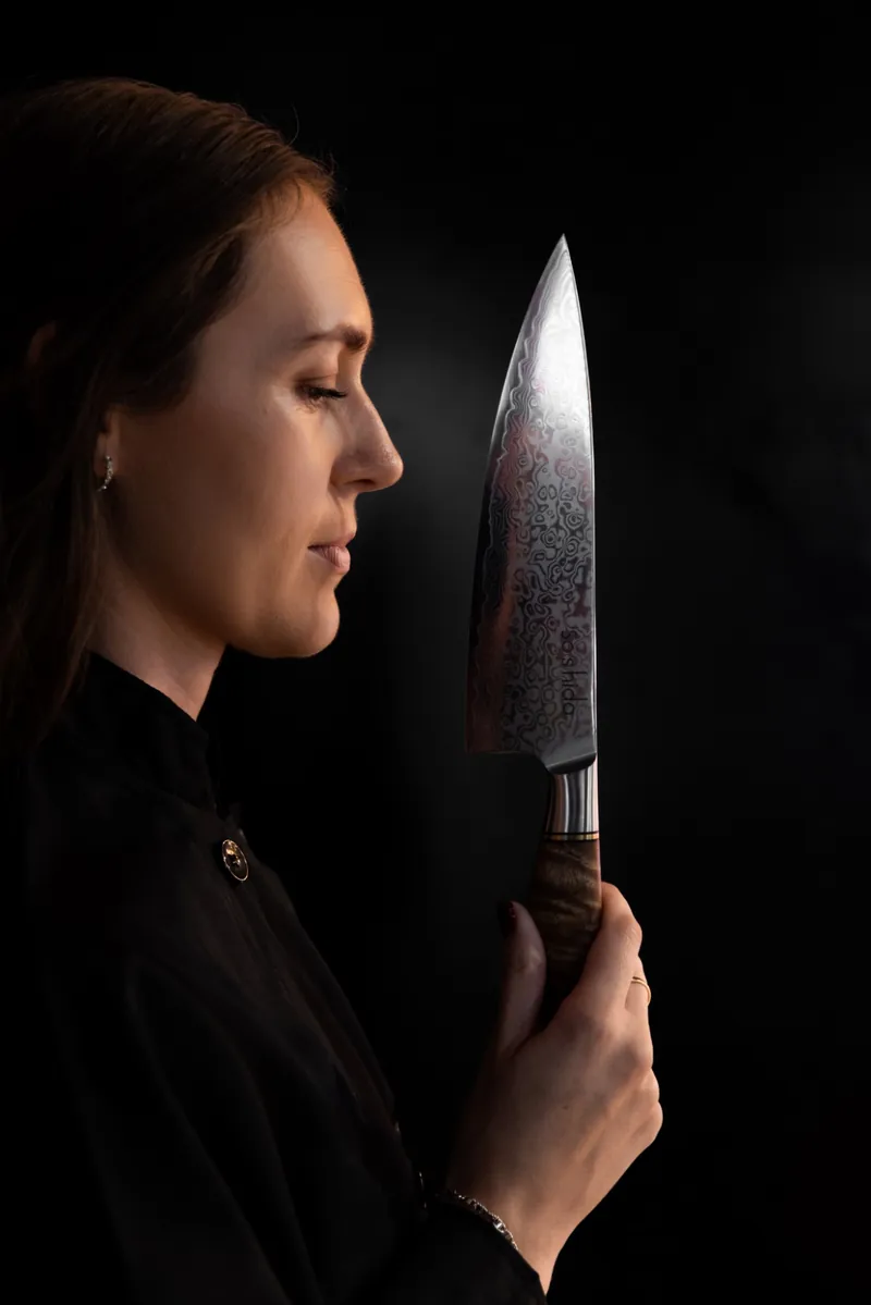A chef in profile holding a Soshida Damascus steel chef's knife upright against a black background