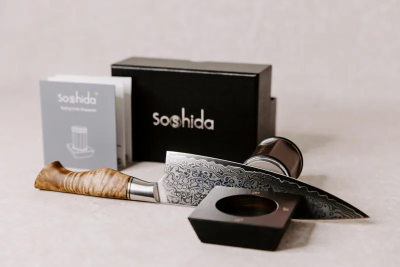 Soshida Damascus steel chef's knife and rolling knife sharpener in front of the black Soshida gift box